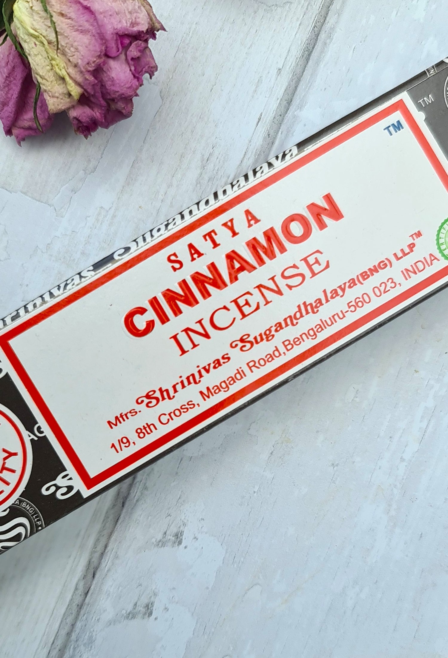 Box of Satya Cinnamon incense on a light wooden surface with pink flowers.