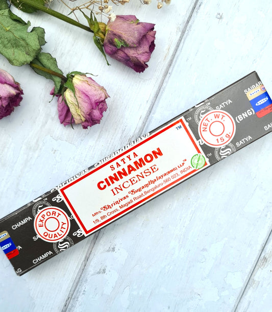 Satya Cinnamon incense stick box on a wooden surface with dried roses.