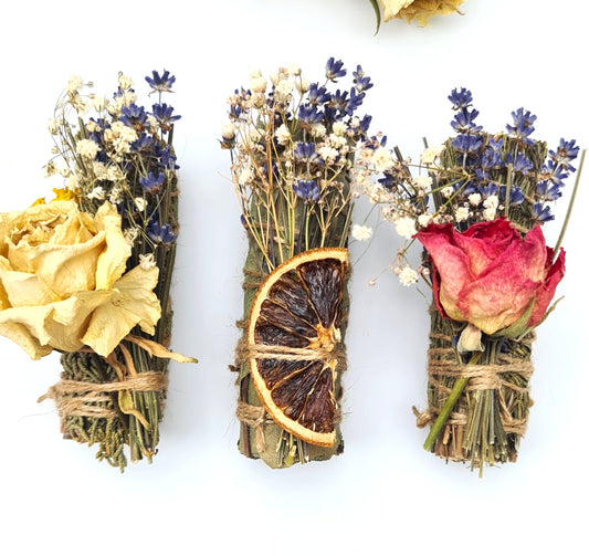 Three bundles of dried flowers and herbs tied with twine on a white background