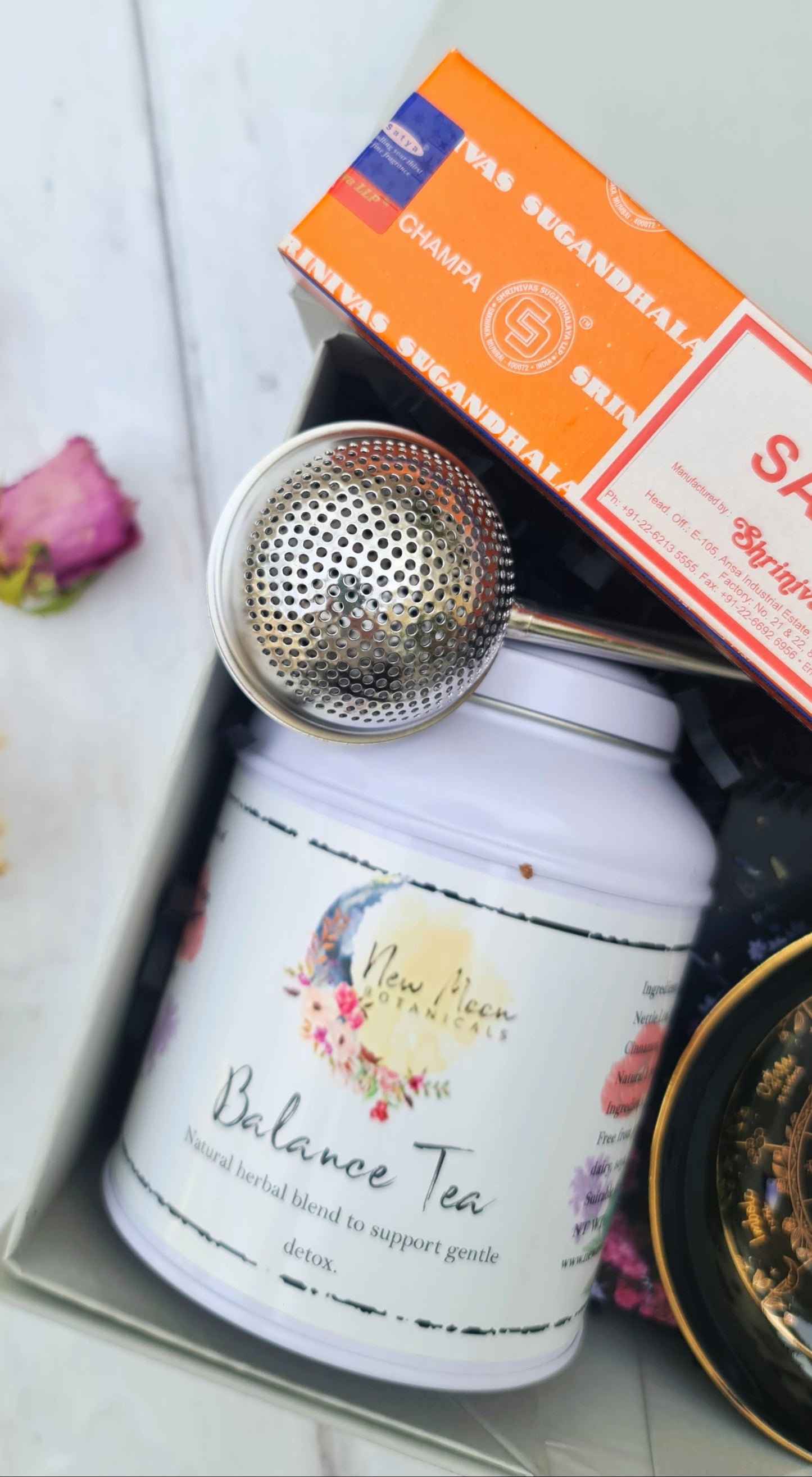 Tea canister with a strainer, pink flower, and boxes on a white surface