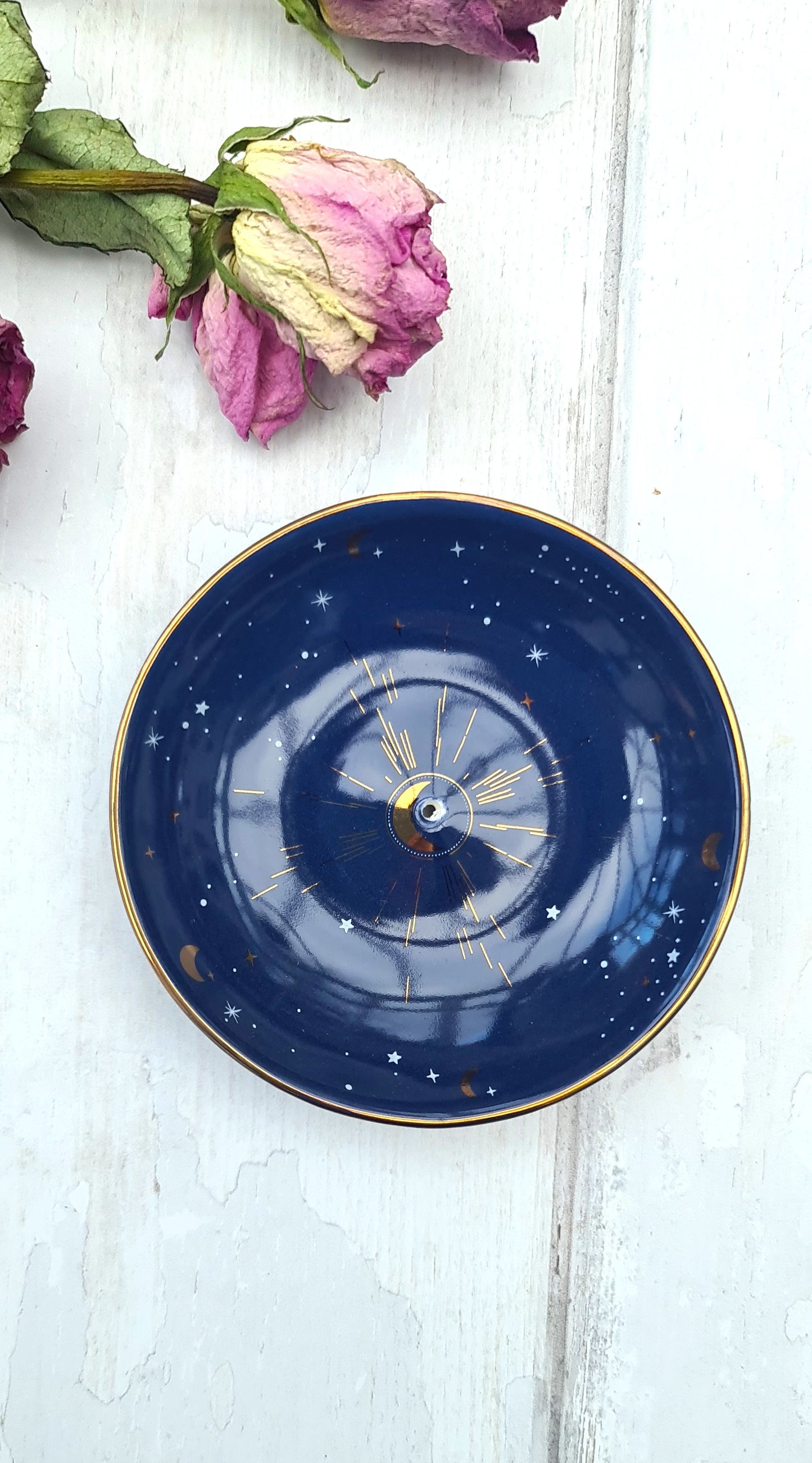 Blue ceramic plate with gold rim on a white wooden surface with dried pink roses.