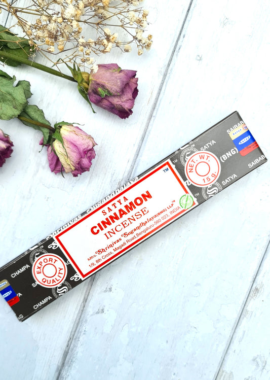 Satya Cinnamon incense packaging on a white surface with dried flowers.