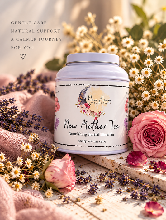 A jar of New Moon Botanicals New Mother Tea is styled on a rustic wooden surface surrounded by pink roses, lavender, and small white daisies, with soft pink fabric and a warm, sunlit background.