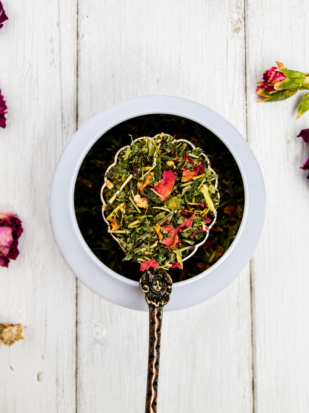 Tea leaves with flowers in a white dish on a wooden surface