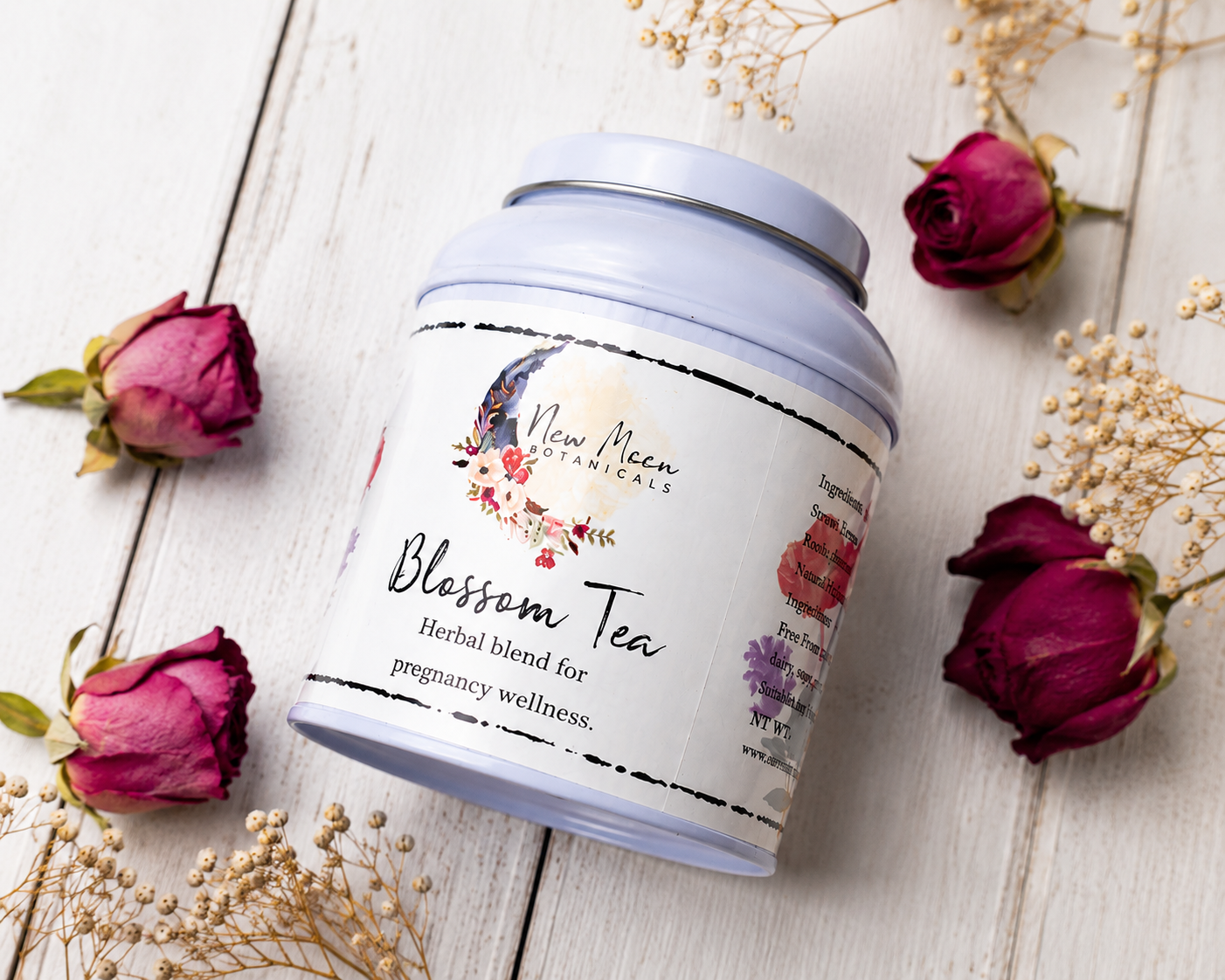 Tea canister labeled 'Blossom Tea' with floral design on a wooden surface with dried roses.