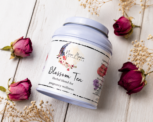 Tea canister labeled 'Blossom Tea' with floral design on a wooden surface with dried roses.
