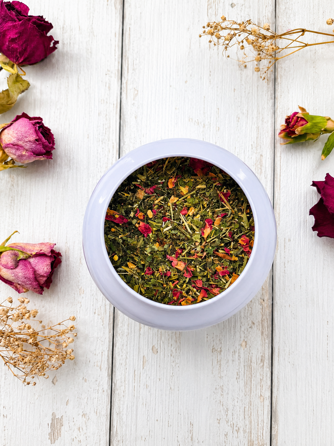 White bowl filled with colorful dried flowers on a wooden surface with dried roses and gypsophila.