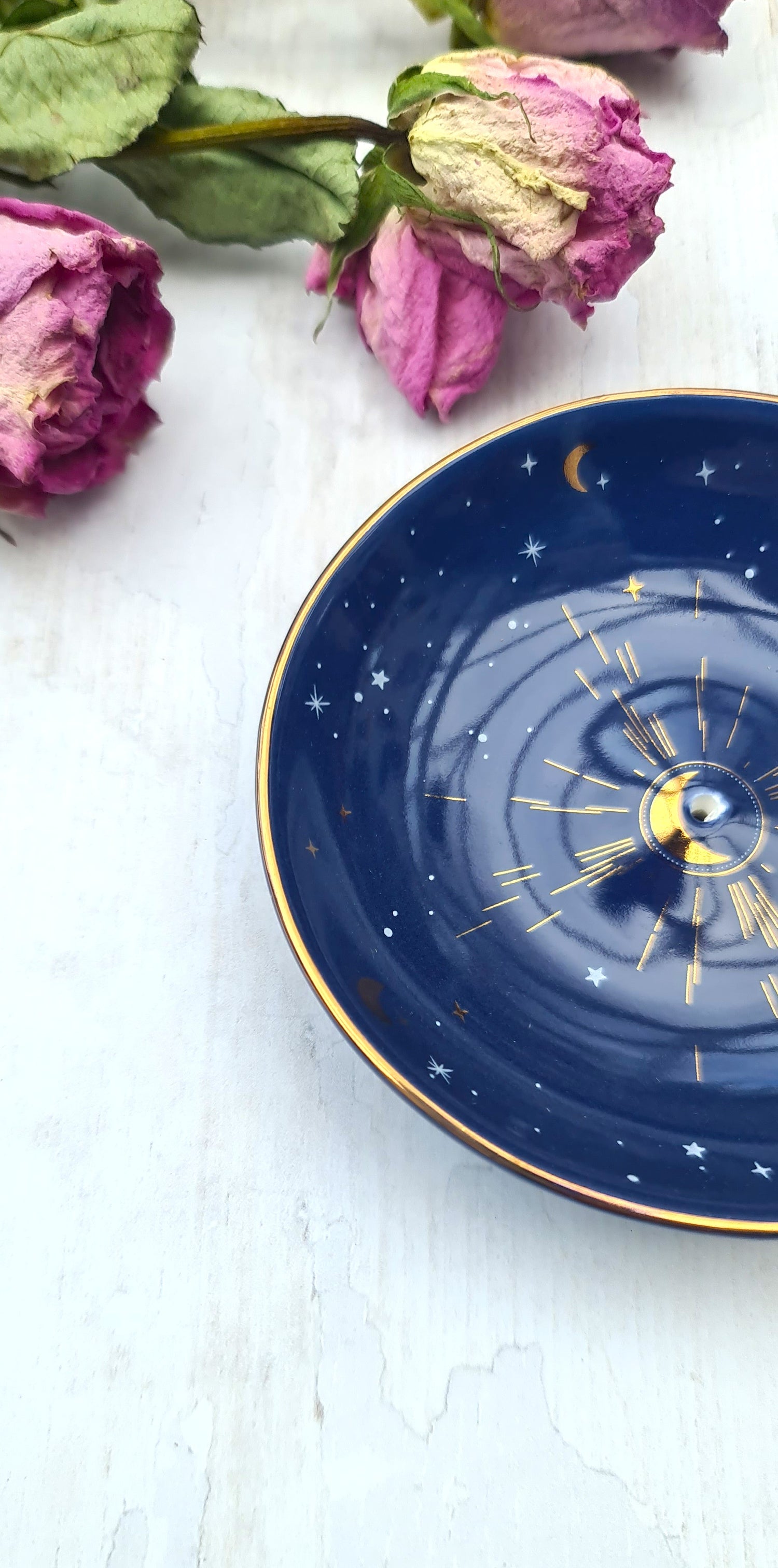 Navy blue decorative plate with celestial design on a white surface with dried pink roses.