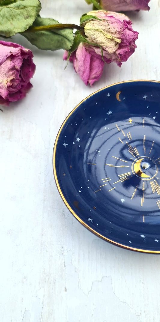 Navy blue decorative plate with celestial design on a white surface with dried pink roses.